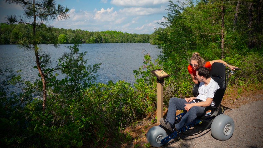 A man in an all-terrain wheelchair visiting Atsion Recreation Area with a companion.