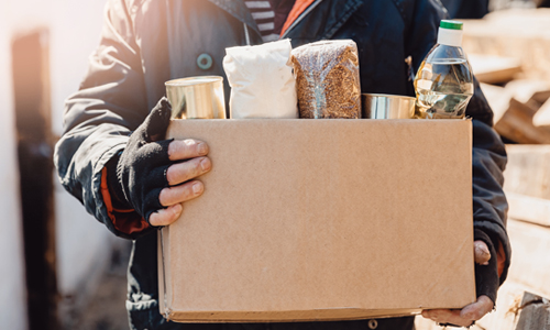 Person carrying a cardboard box filled with groceries