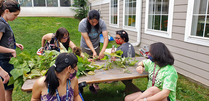J-Cares interns and staff at a picnic table piled with leafy green plants at the Jewish Community Center