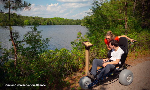 A man in an all-terrain wheelchair visiting Atsion Recreation Area with a companion.